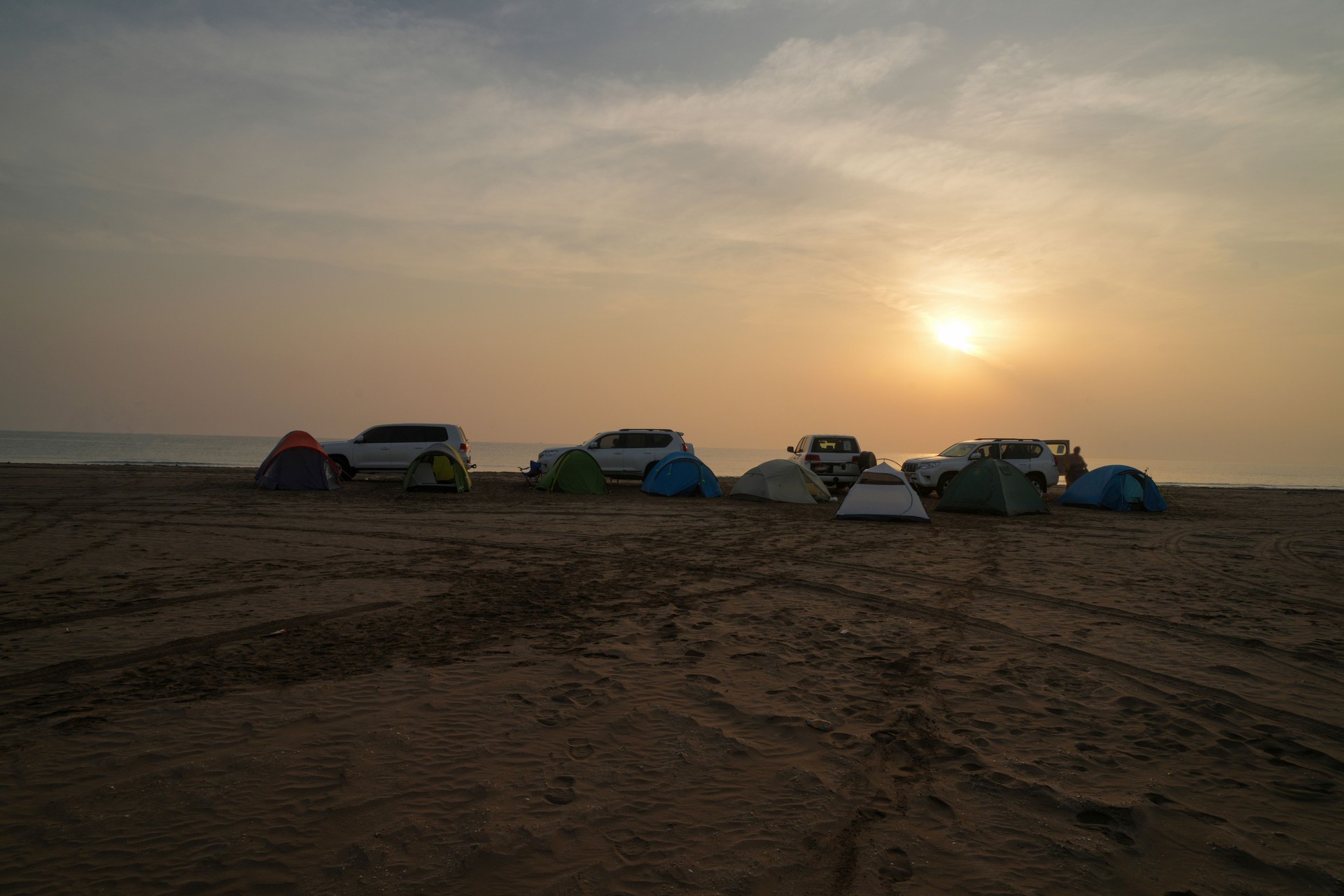 Morning, with sunrise above Small group of tourists camping on sand beach, with tent and cars on the top of small dune, Oman.